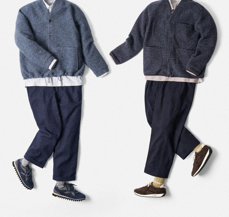 To fladlagte outfits fra Universal Works: uldcardigans i mørkeblå og lyseblå, hvid skjorte, blå bukser og sneakers.